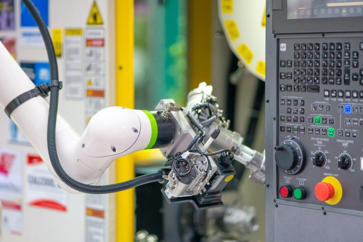 Collaborative robot arm connected to a CNC machine control panel on the factory floor